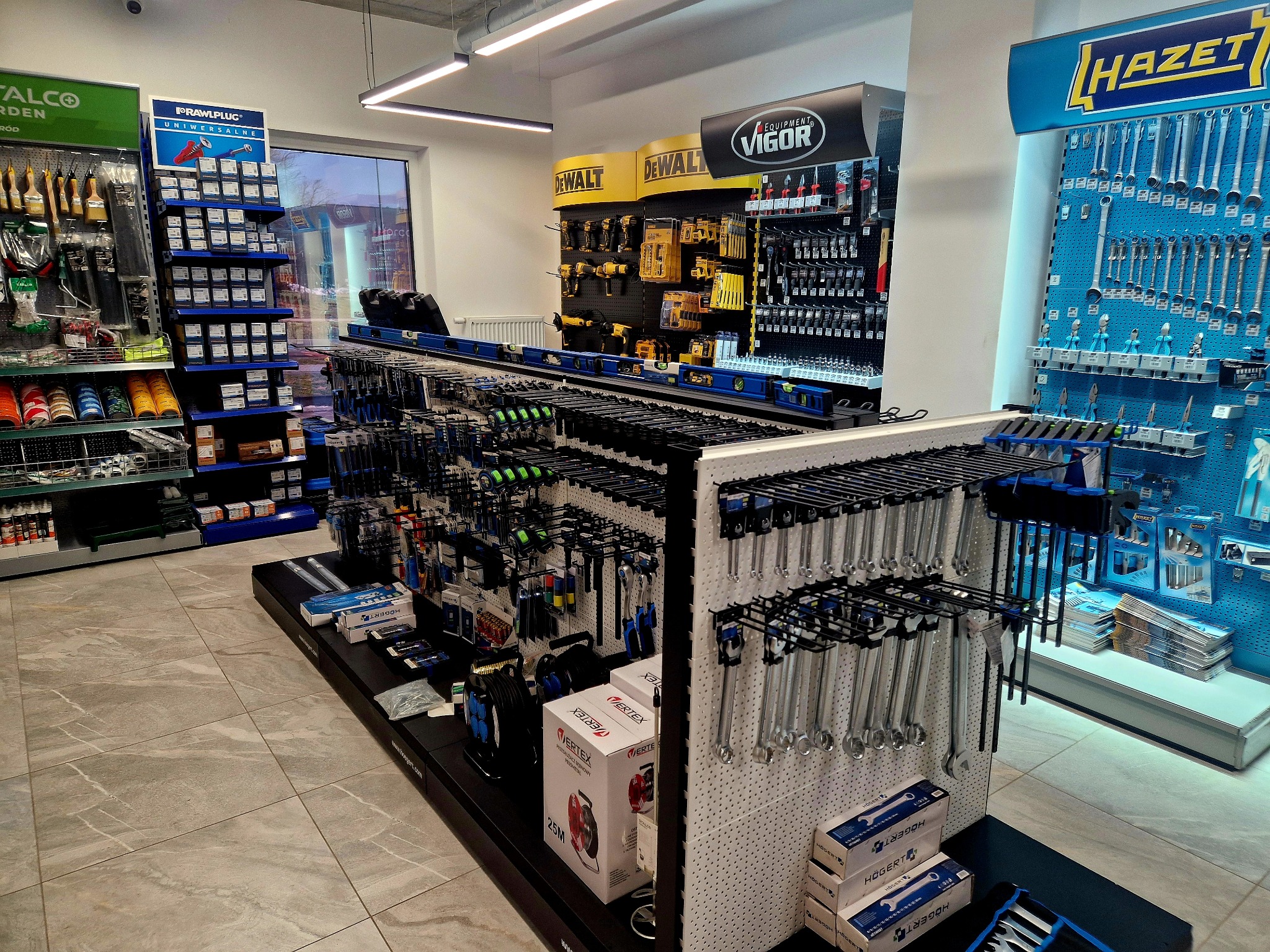 Wnętrze sklepu z narzędziami: ekspozycja marek DeWalt, Hazet, Vigor, Rawlplug i Metalco. Szeroki wybór narzędzi ręcznych i elektronarzędzi na półkach i ścianach.
