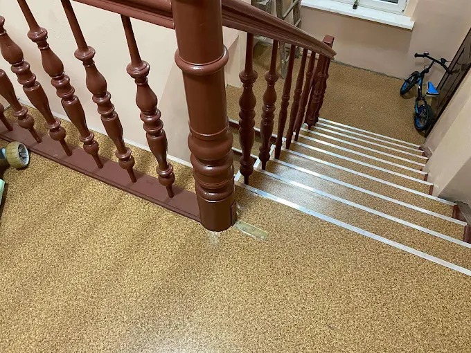 Schody wyłożone wykładziną korkową z metalowymi listwami antypoślizgowymi. Ciemne, drewniane poręcze. W tle rower dziecięcy.