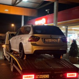 Mykyta Oleshchenko DM Company - Srebrne BMW kombi na platformie lawety, widok z tyłu, nocne oświetlenie, tablice rejestracyjne widoczne. Auto z czarnymi felgami.