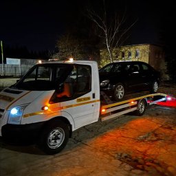 Mykyta Oleshchenko DM Company - Nocny transport czarnego samochodu osobowego na lawecie pomocy drogowej. Biały bus z żółtymi pasami i napisem 'Pomoc Drogowa'.