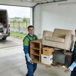 GALPA PAWEŁ BIAŁOŃ - Dwóch mężczyzn w kombinezonach niesie na palecie meble i sprzęt RTV. W tle biały bus z otwartymi drzwiami załadowany różnymi przedmiotami. Opróżnianie pomieszczenia.