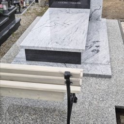 Kamieniarstwo Artystyczne Jacek Kociołek - Granitowy nagrobek z czarną tablicą i jasnoszarą płytą, uzupełniony o ławkę. Widoczny krzyż i daty na tablicy. Całość na cmentarzu, z logo firmy w rogu.
