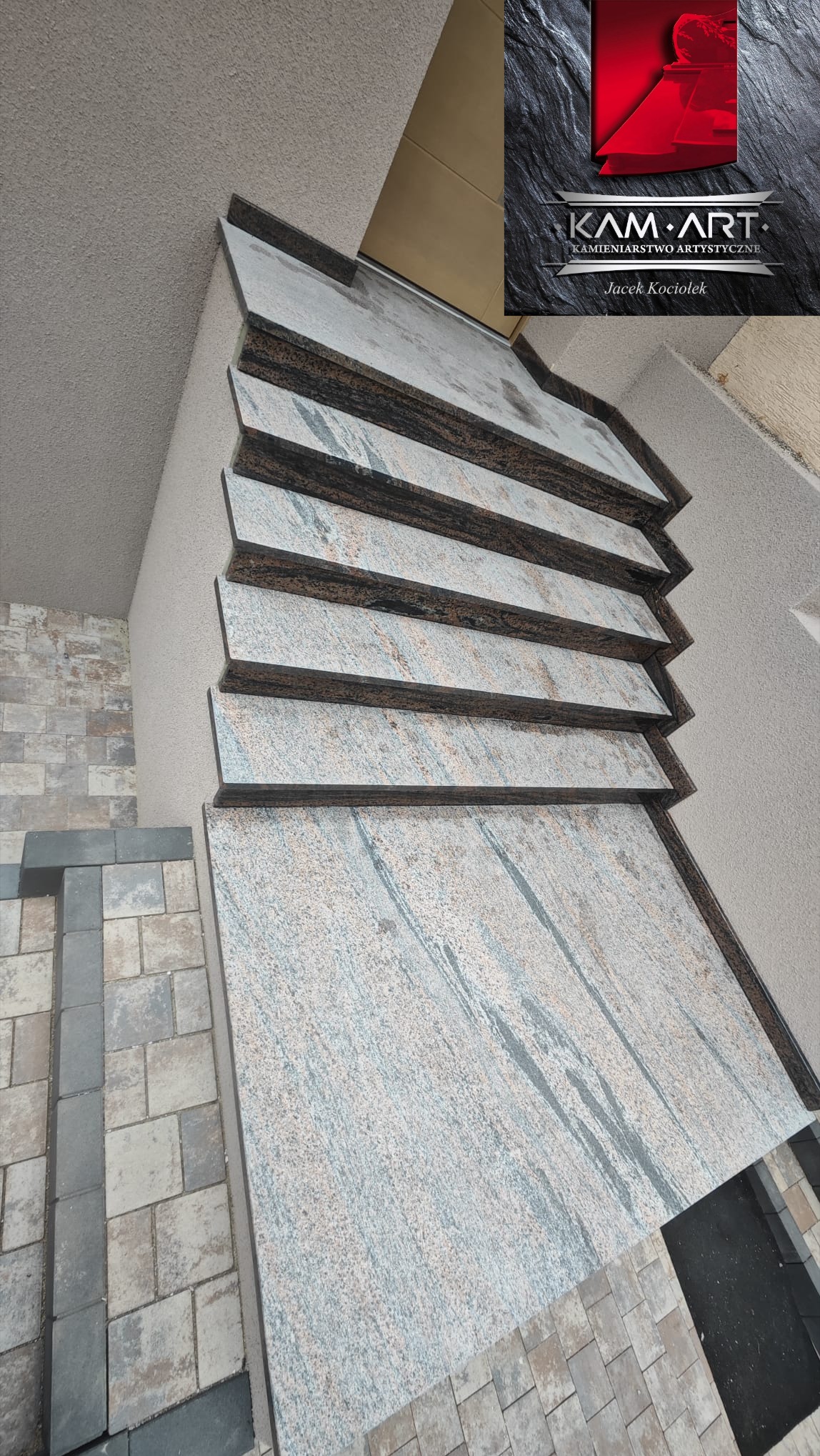 Kamienne schody zewnętrzne z jasnego granitu z ciemnymi krawędziami, prowadzące do wejścia. Widoczna kostka brukowa i logo firmy kamieniarskiej.