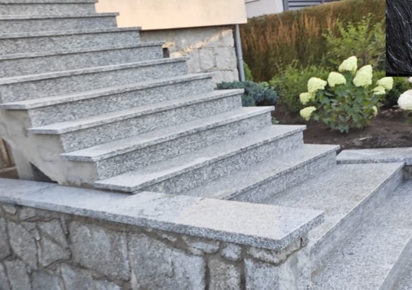 Zewnętrzne schody z jasnoszarego granitu, prowadzące do domu. Widoczne detale wykończenia i otoczenie z zielenią. Ujęcie z dołu, podkreślające solidność konstrukcji.