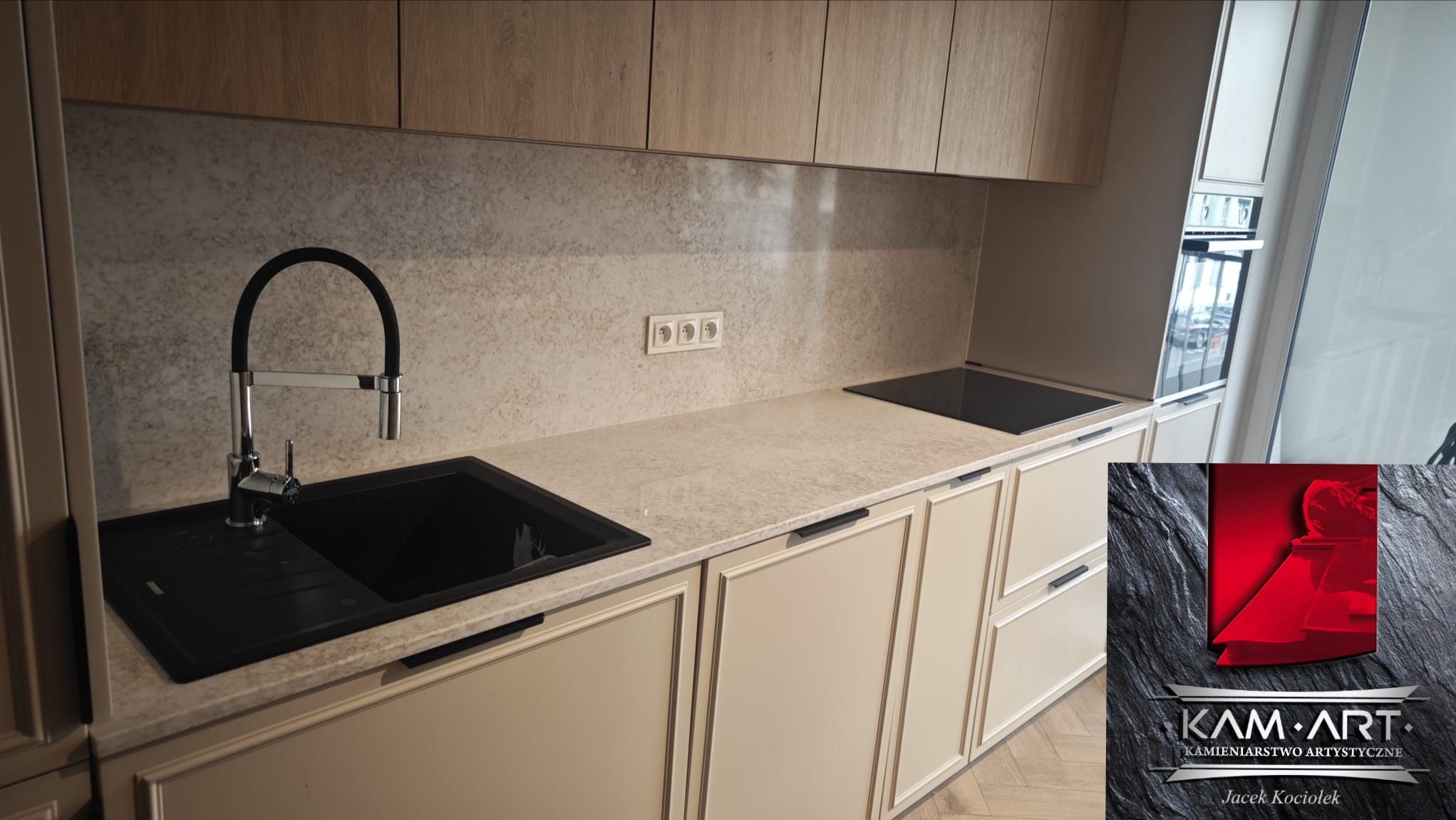 Jasny blat kamienny z czarnym zlewem i płytą grzewczą w nowoczesnej kuchni. Uwagę przykuwa subtelny wzór kamienia i minimalistyczne uchwyty szafek.