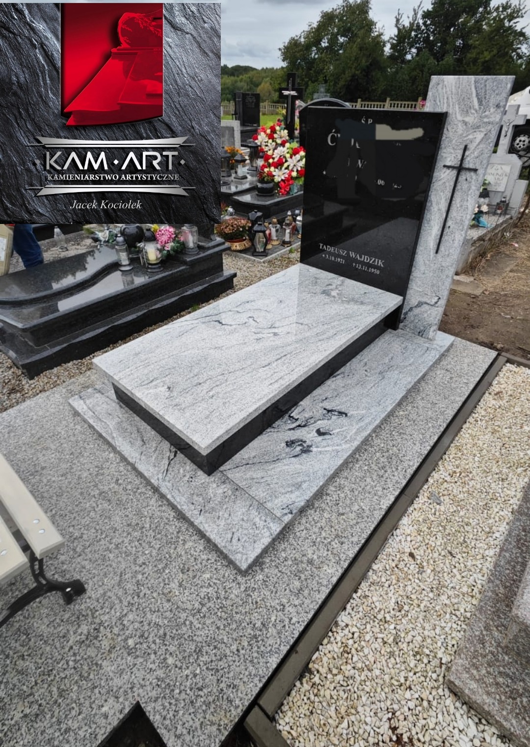 Nowoczesny nagrobek z jasnego granitu z czarną tablicą i krzyżem, otoczony innymi nagrobkami na cmentarzu. Widoczne logo firmy Kam-Art.