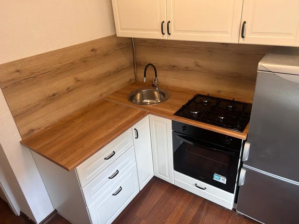 Jasna kuchnia z drewnianym blatem i białymi szafkami. Uwagę przykuwa kompaktowa zabudowa z piekarnikiem i płytą gazową, idealna do małych przestrzeni.