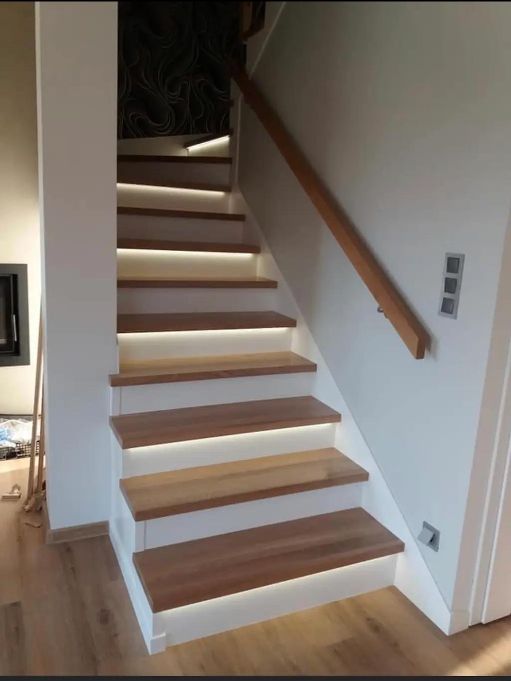 Nowoczesne schody drewniane z subtelnym podświetleniem LED, białe ściany, drewniana poręcz. Minimalistyczny design z akcentem na oświetlenie.