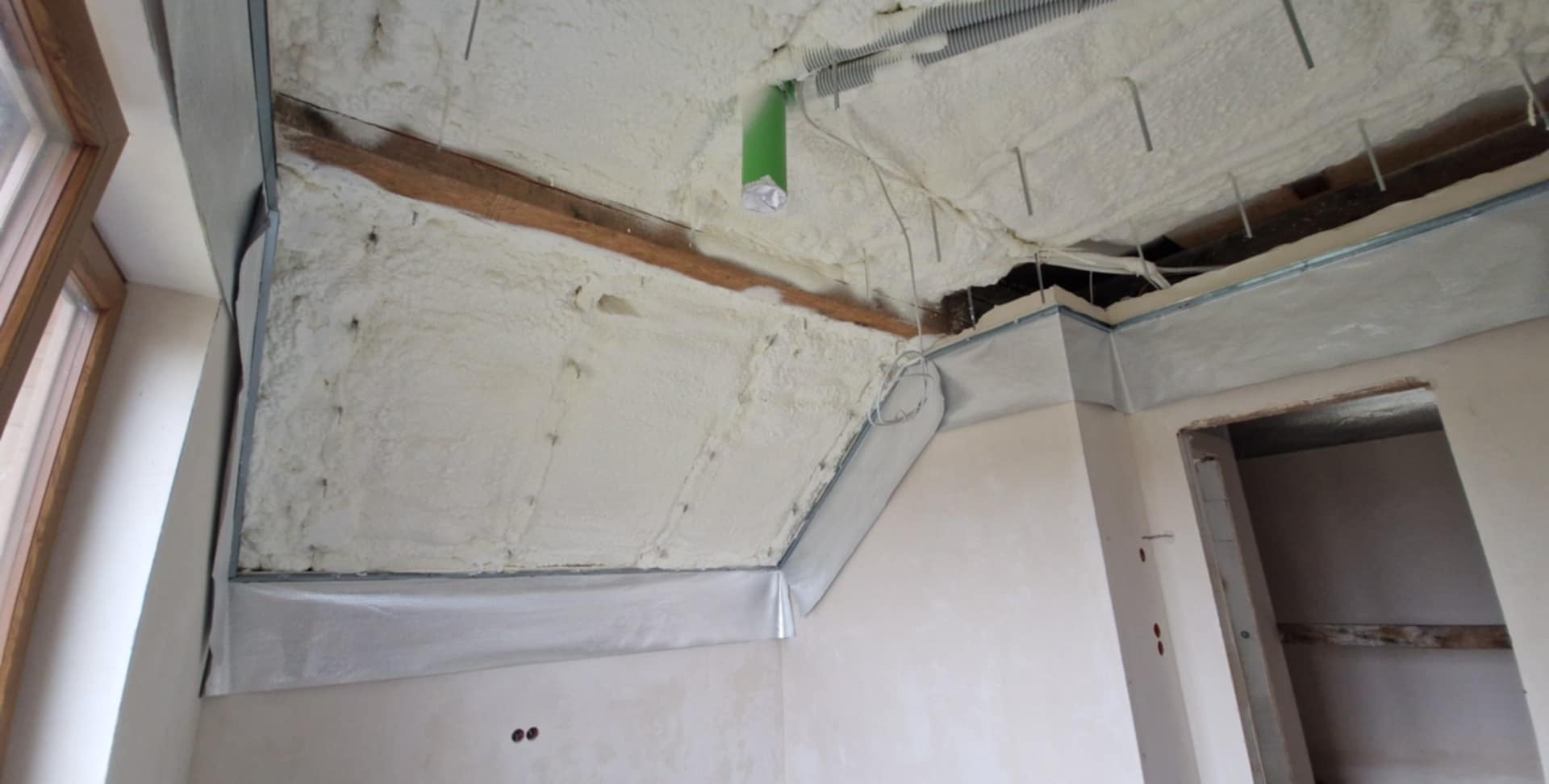 Poddasze po natrysku pianki izolacyjnej, widoczne drewniane elementy konstrukcyjne i metalowe profile. Częściowo wykończone ściany i przygotowane do dalszych prac.