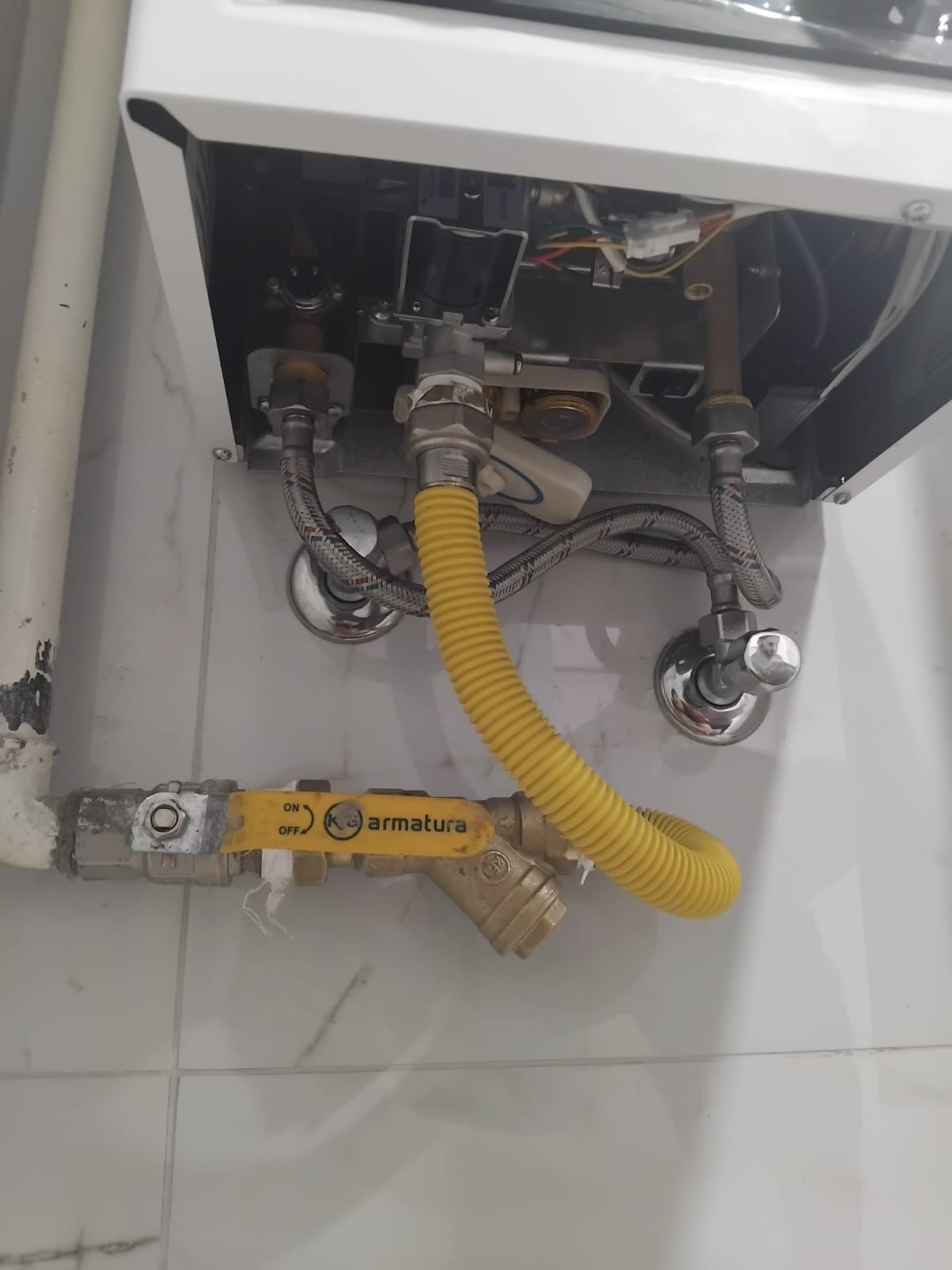 Żółty przewód gazowy Armatura łączy piec z instalacją. Widoczne zawory i rury na tle białych płytek. Ujęcie z bliska, skupione na połączeniach.