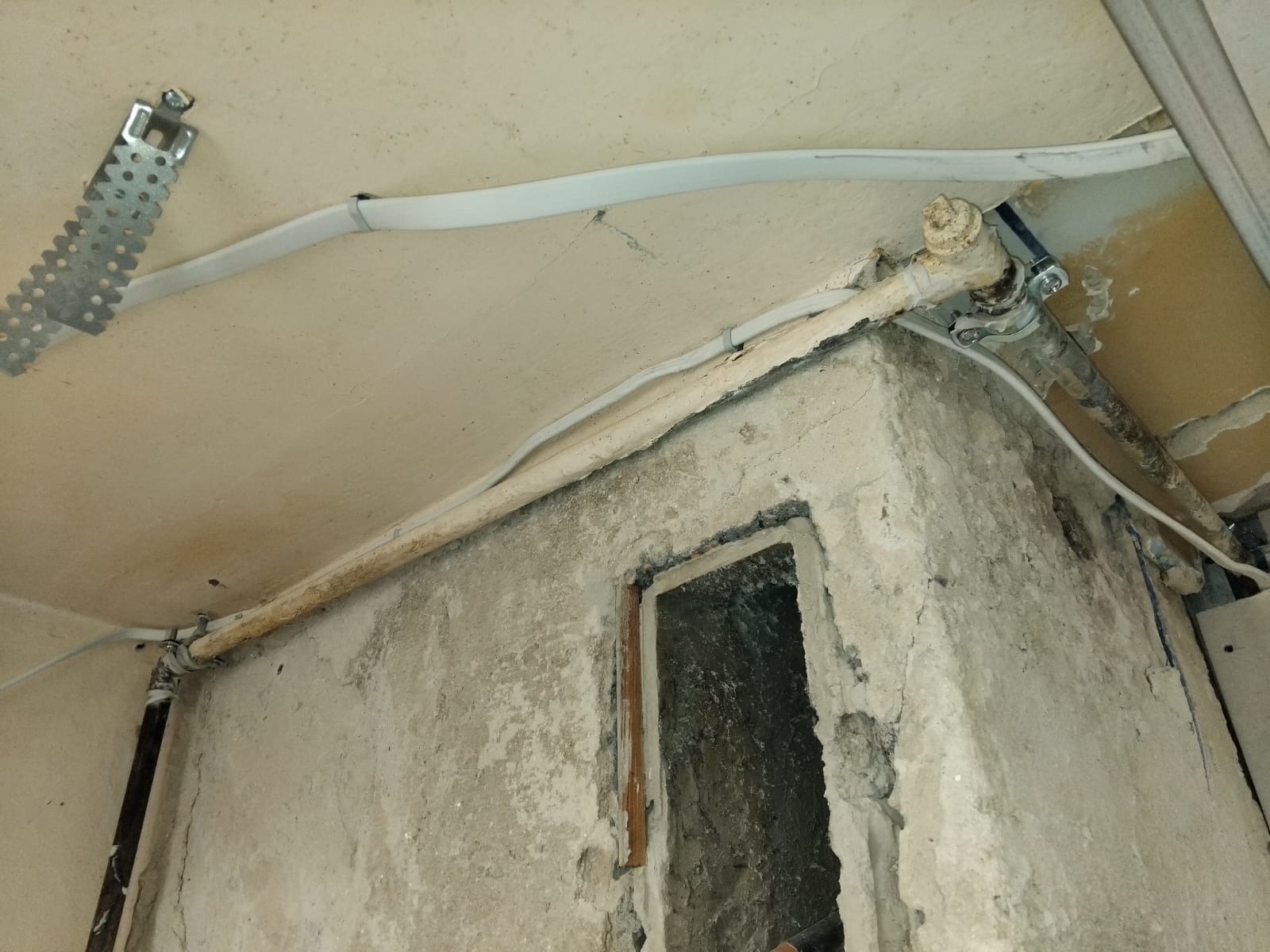 Fragment instalacji gazowej z rurami biegnącymi wzdłuż ściany i pod sufitem, widoczne mocowania i elementy przyłączeniowe. Surowy stan wykończenia ścian.