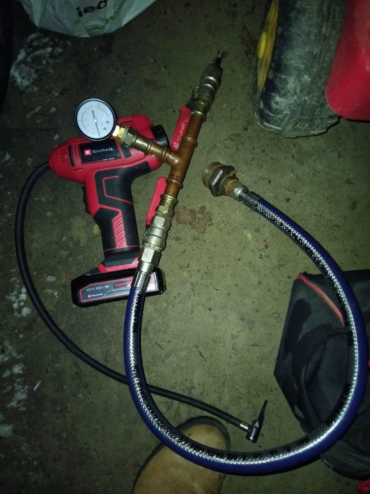 Narzędzie do pomiaru ciśnienia gazu z manometrem i elektryczną pompką Einhell, leżące na szarej powierzchni. Widoczne złączki i węże.