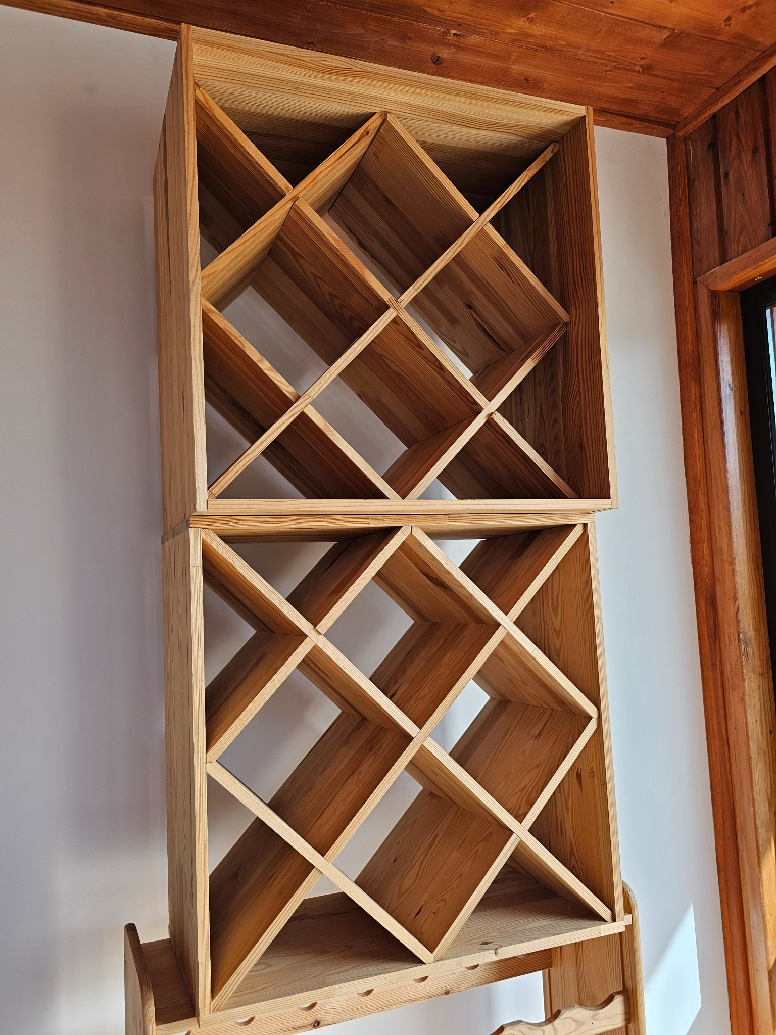 Drewniany regał z kwadratowymi przegródkami, ustawiony na tle białej ściany i drewnianej boazerii. Widoczne naturalne usłojenie drewna i precyzyjne wykonanie.