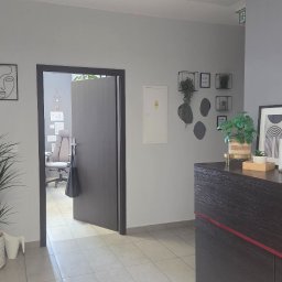 DLF PLACE sp. z o.o. - Nowoczesne biuro po sprzątaniu: minimalistyczny wystrój, rośliny doniczkowe, czyste podłogi i recepcja z dekoracjami. Widoczny otwarty pokój biurowy w tle.