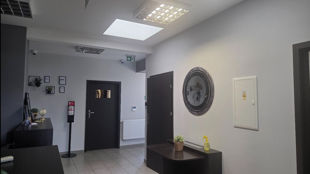 Wnętrze biura po sprzątaniu: czyste podłogi, zadbane meble, lustro na ścianie, dozownik z płynem dezynfekującym, schludne dekoracje i oświetlenie.