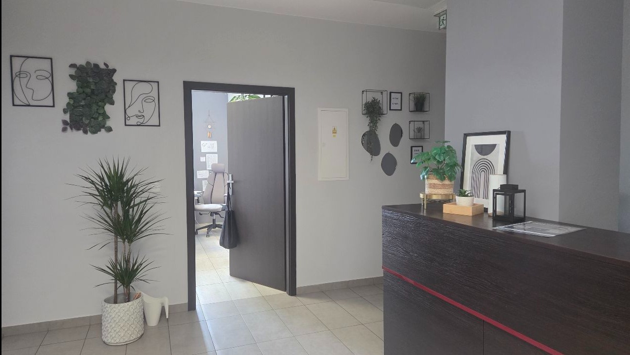 Nowoczesne biuro po sprzątaniu: minimalistyczny wystrój, rośliny doniczkowe, czyste podłogi i recepcja z dekoracjami. Widoczny otwarty pokój biurowy w tle.