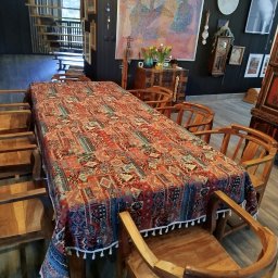 Patrycja Simińska - Ustawiony stół z wzorzystym obrusem w przestronnym wnętrzu w Łodzi. Drewniane krzesła i schody w tle. Dekoracje na ścianie dodają charakteru.