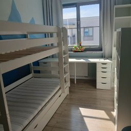 Patrycja Simińska - Pokój dziecięcy po sprzątaniu: białe łóżko piętrowe, biurko z zabawkami przy oknie, regał. Czyste, jasne wnętrze z drewnianą podłogą.