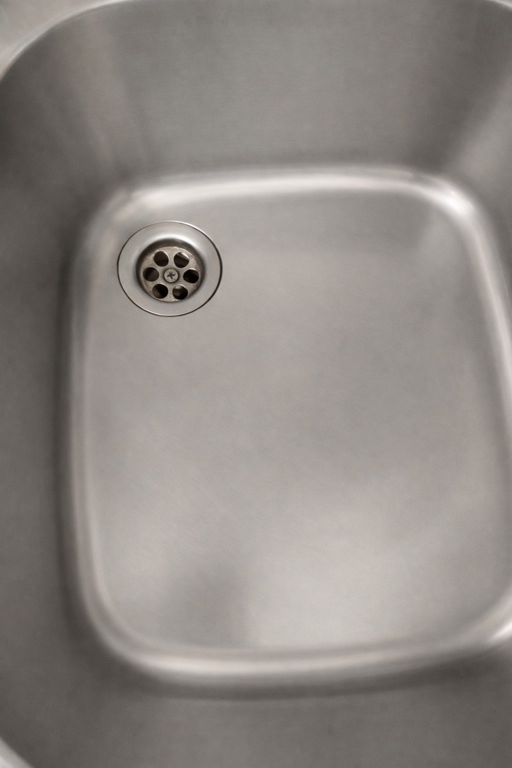 Błyszczący, czysty zlew ze stali nierdzewnej z widocznym odpływem. Minimalistyczne ujęcie z góry, ukazujące gładką powierzchnię i higieniczny wygląd.