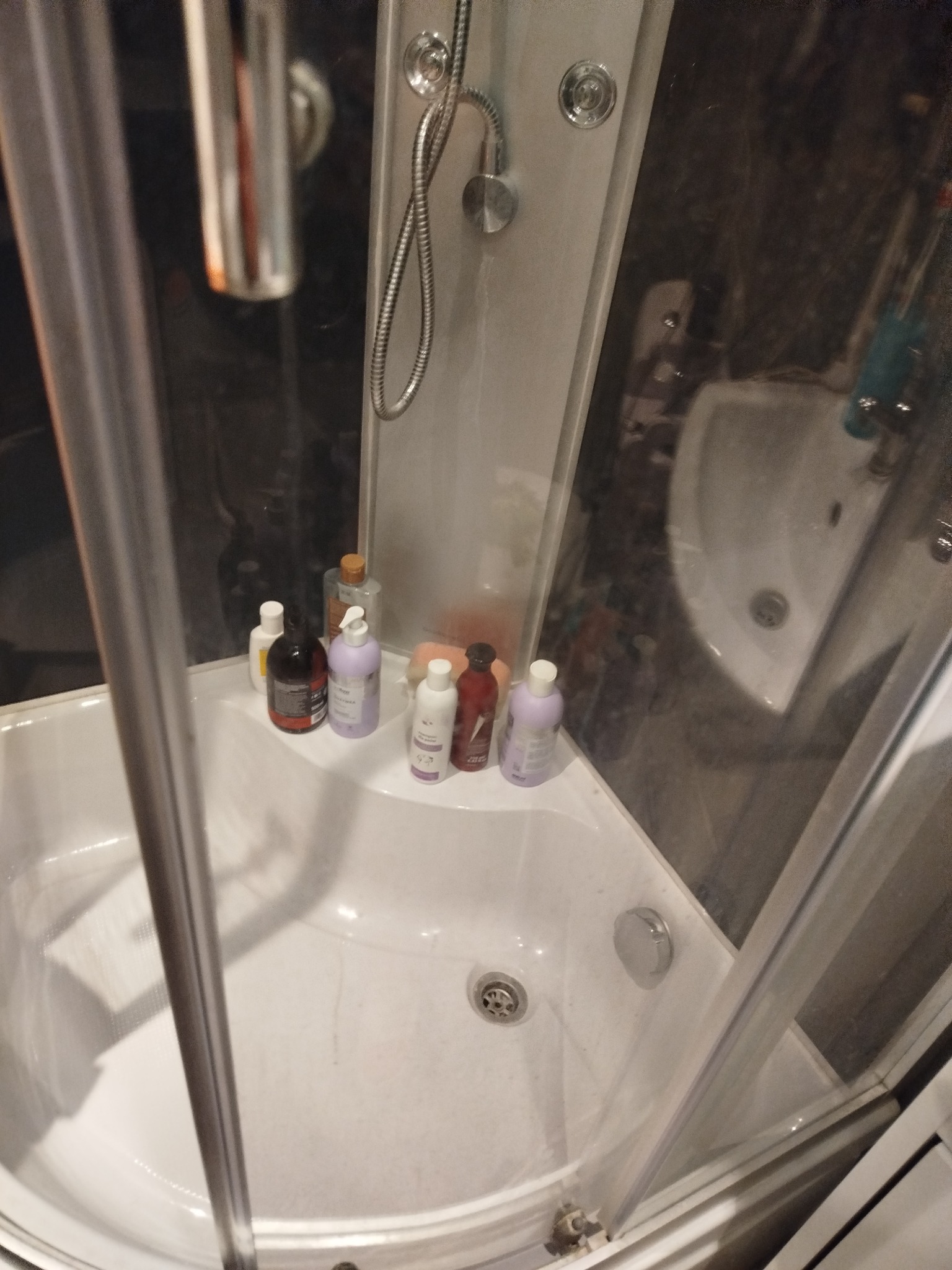 Wnętrze kabiny prysznicowej z widocznymi butelkami kosmetyków i armaturą. Ujęcie z góry, ukazujące czystość i porządek w przestrzeni kąpielowej.