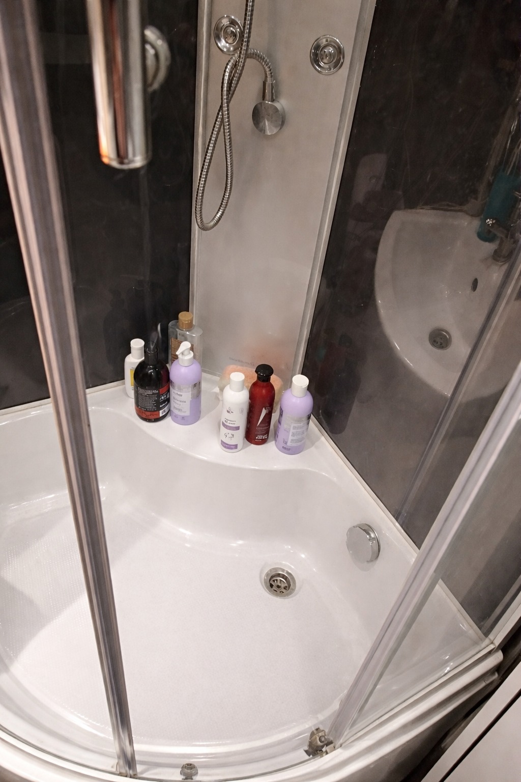 Wnętrze kabiny prysznicowej z kosmetykami na półce, widok z góry, czysta armatura i umywalka w tle. Sprzątanie łazienki po remoncie.