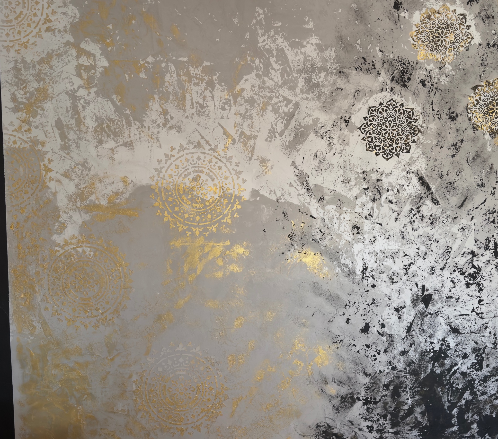 Dekoracyjna ściana z efektem ombre w odcieniach szarości, złota i czerni. Na powierzchni widoczne wzory mandali w kolorze złotym i czarnym, tworzące unikalną teksturę.