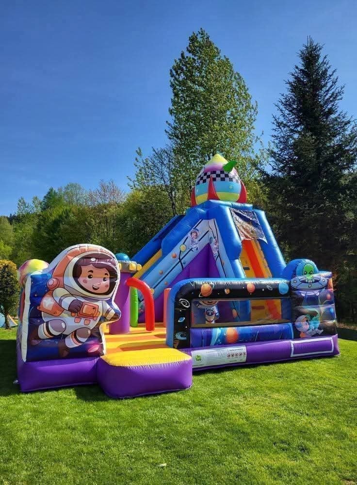 Kolorowy dmuchany zamek w kosmicznym stylu z motywem astronauty i rakiety na tle zieleni i błękitnego nieba, idealny na imprezy plenerowe dla dzieci.