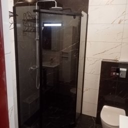 PAWEX - Nowoczesna kabina prysznicowa z czarną ramą i deszczownicą, w łazience wykończonej płytkami imitującymi marmur w odcieniach bieli i czerni. Widoczna toaleta i umywalka.