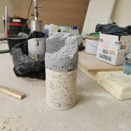 DIAMCORE - Rdzenie betonu po wierceniu, widoczne narzędzia i materiały budowlane w pomieszczeniu. Próbki betonu o różnej strukturze, wiertnica w tle.