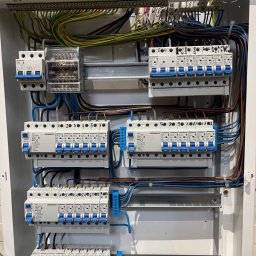 Luxel - Rozdzielnica elektryczna z zainstalowanymi bezpiecznikami i okablowaniem. Widoczne przewody w różnych kolorach i oznaczenia na elementach.