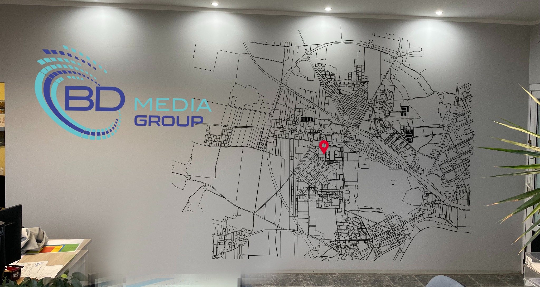 Ściana biura z logo 'BD Media Group' i mapą miasta z czerwoną pinezką. Nowoczesny design wnętrza, jasne oświetlenie, minimalistyczny styl.