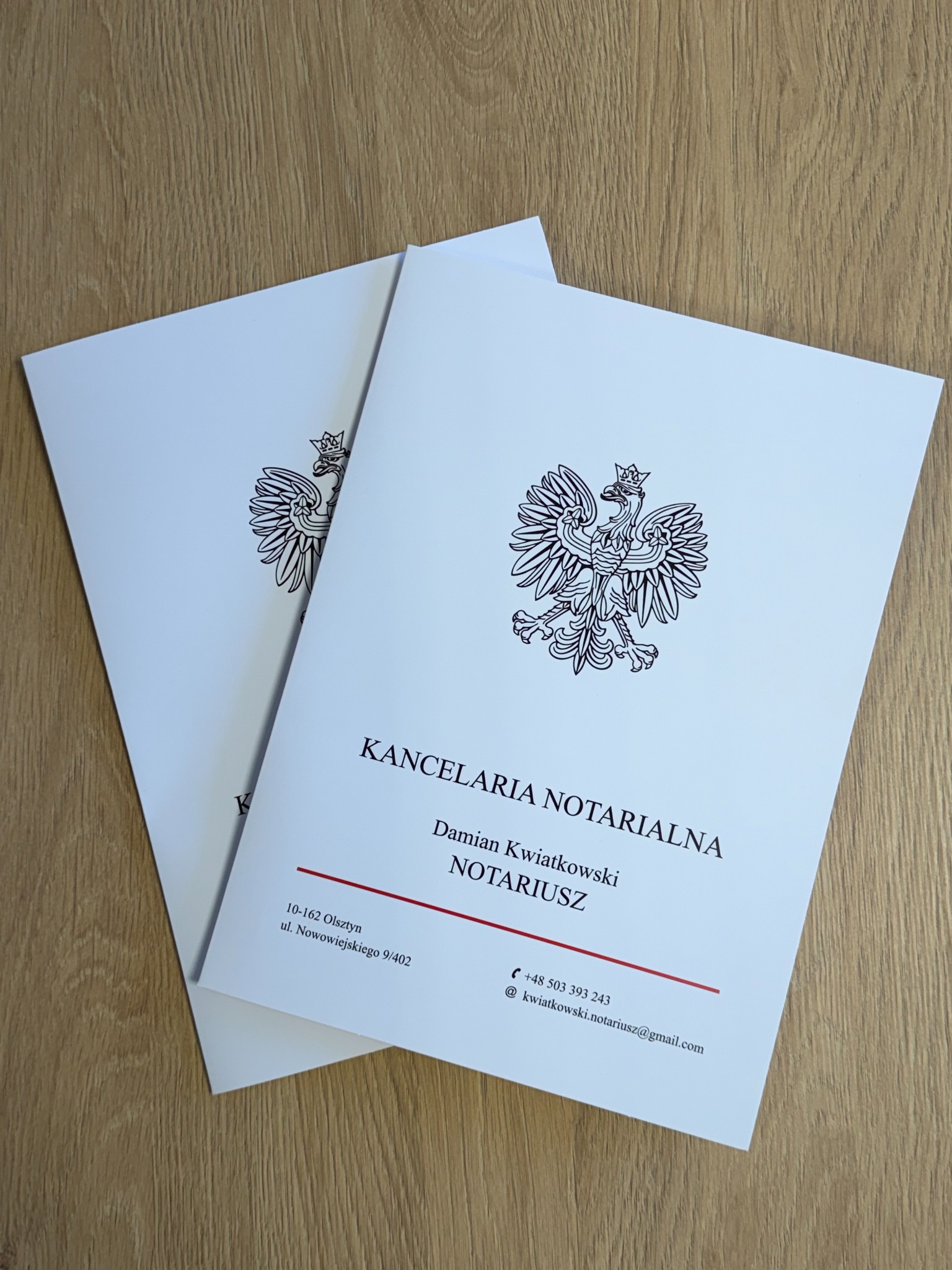 Dwa dokumenty Kancelarii Notarialnej z godłem Polski, leżące na drewnianym biurku. Widoczny adres i dane kontaktowe notariusza Damiana Kwiatkowskiego.
