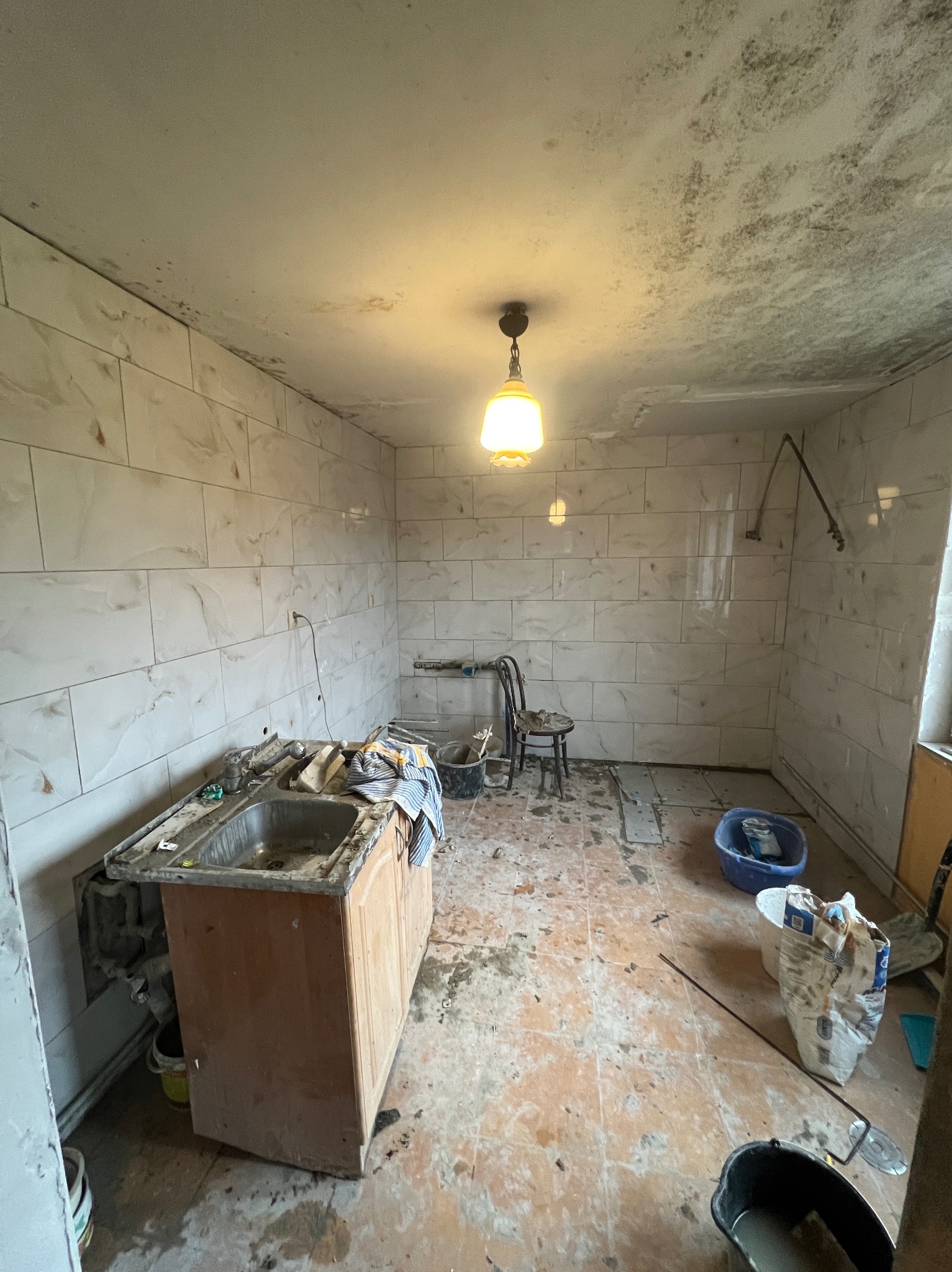 Remont łazienki: świeżo położone, marmurkowe płytki ścienne kontrastują z brudną podłogą i starą umywalką. Widoczne narzędzia i materiały budowlane.