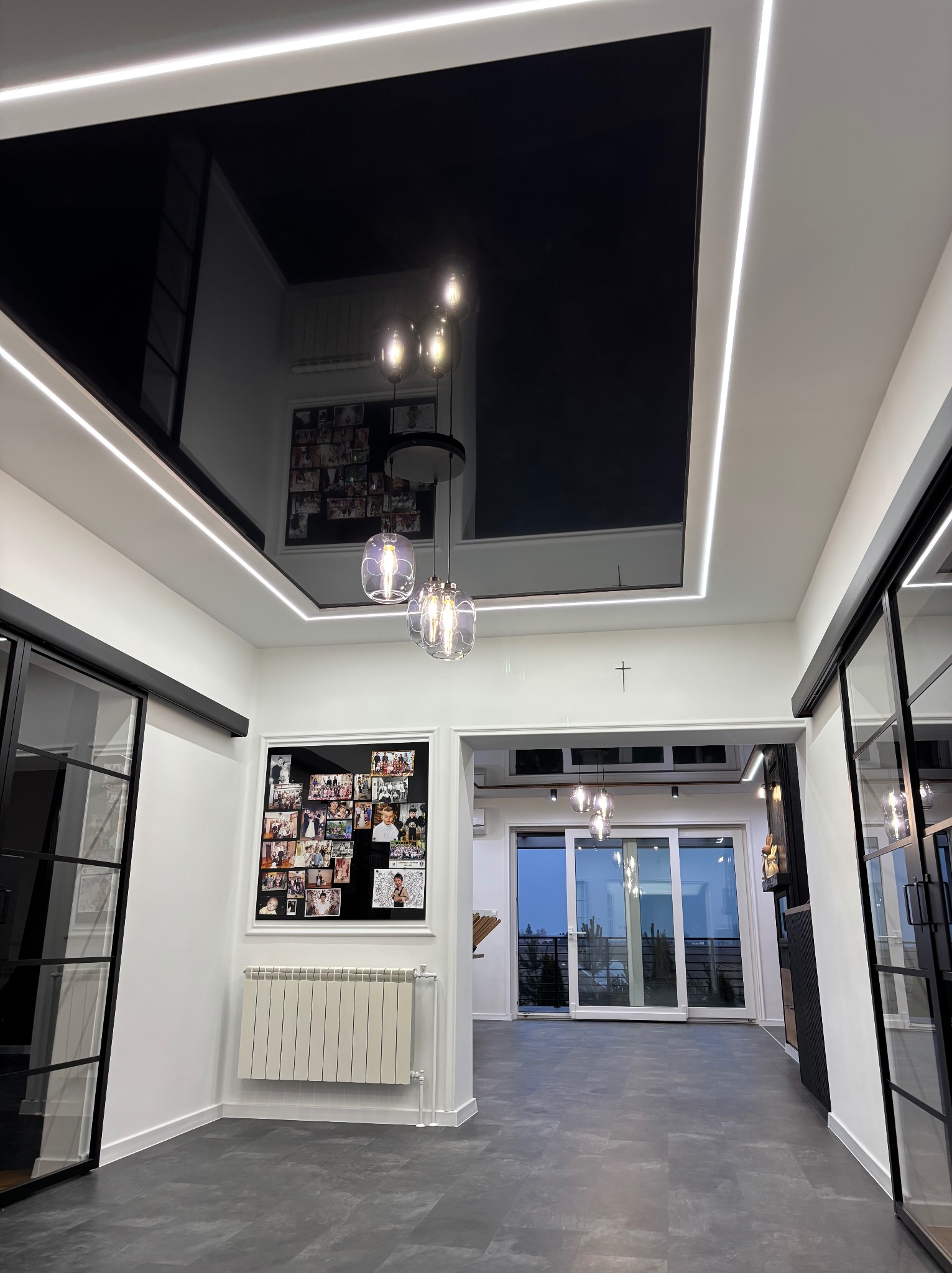 Nowoczesne wnętrze z czarnym, lustrzanym sufitem podwieszanym i oświetleniem LED. Widoczne szklane lampy wiszące i przesuwne drzwi.