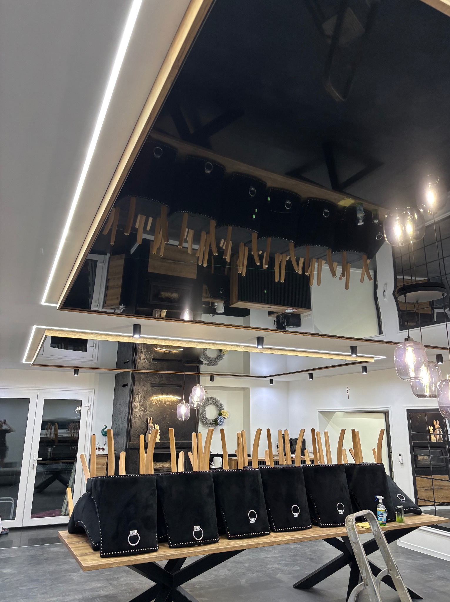 Nowoczesne wnętrze z czarnym, lustrzanym sufitem podwieszanym i oświetleniem LED. Krzesła ustawione na stole, przygotowane do prac wykończeniowych.