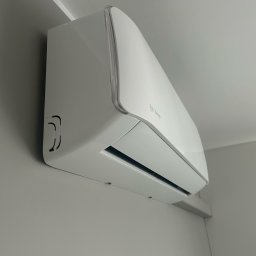 AIR-CTIC MARCIN LUBACZEWSKI - Biały klimatyzator Rotenso zamontowany na szarej ścianie, widok z dołu pod kątem. Minimalistyczny design, nowoczesne wnętrze.