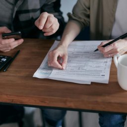 LEVI GROUP SPÓŁKA Z OGRANICZONĄ ODPOWIEDZIALNOŚCIĄ - Wypełnianie formularza podatkowego przy biurku z kalkulatorem, telefonem i kubkiem. Osoby analizują dokumenty, używając długopisu i smartfona.