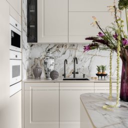 SCM SPÓŁKA Z OGRANICZONĄ ODPOWIEDZIALNOŚCIĄ - Elegancka kuchnia w odcieniach beżu z marmurowym blatem i backsplashiem. Uwagę zwracają dekoracyjne wazony i świeże kwiaty, dodające wnętrzu luksusowego charakteru.