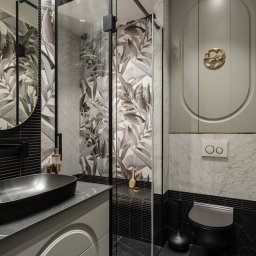 SCM SPÓŁKA Z OGRANICZONĄ ODPOWIEDZIALNOŚCIĄ - Elegancka łazienka z czarną umywalką na szafce z dekoracyjnym, złotym uchwytem, kabiną prysznicową i marmurowymi płytkami z motywem liści.