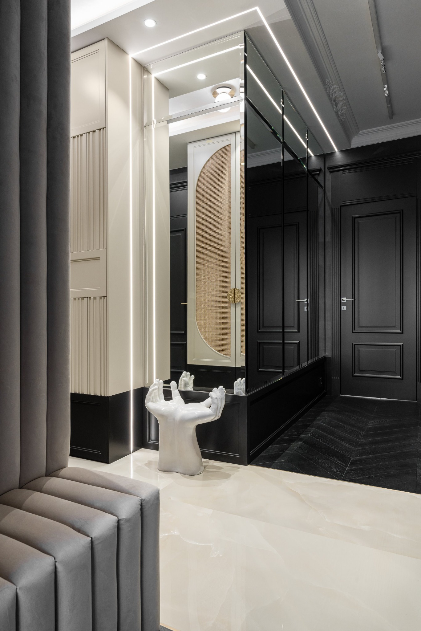 Elegancki przedpokój z lustrzaną szafą, oświetleniem LED i dekoracyjną rzeźbą dłoni. Kontrast bieli i czerni, parkiet w jodełkę, marmurowe płytki podłogowe.