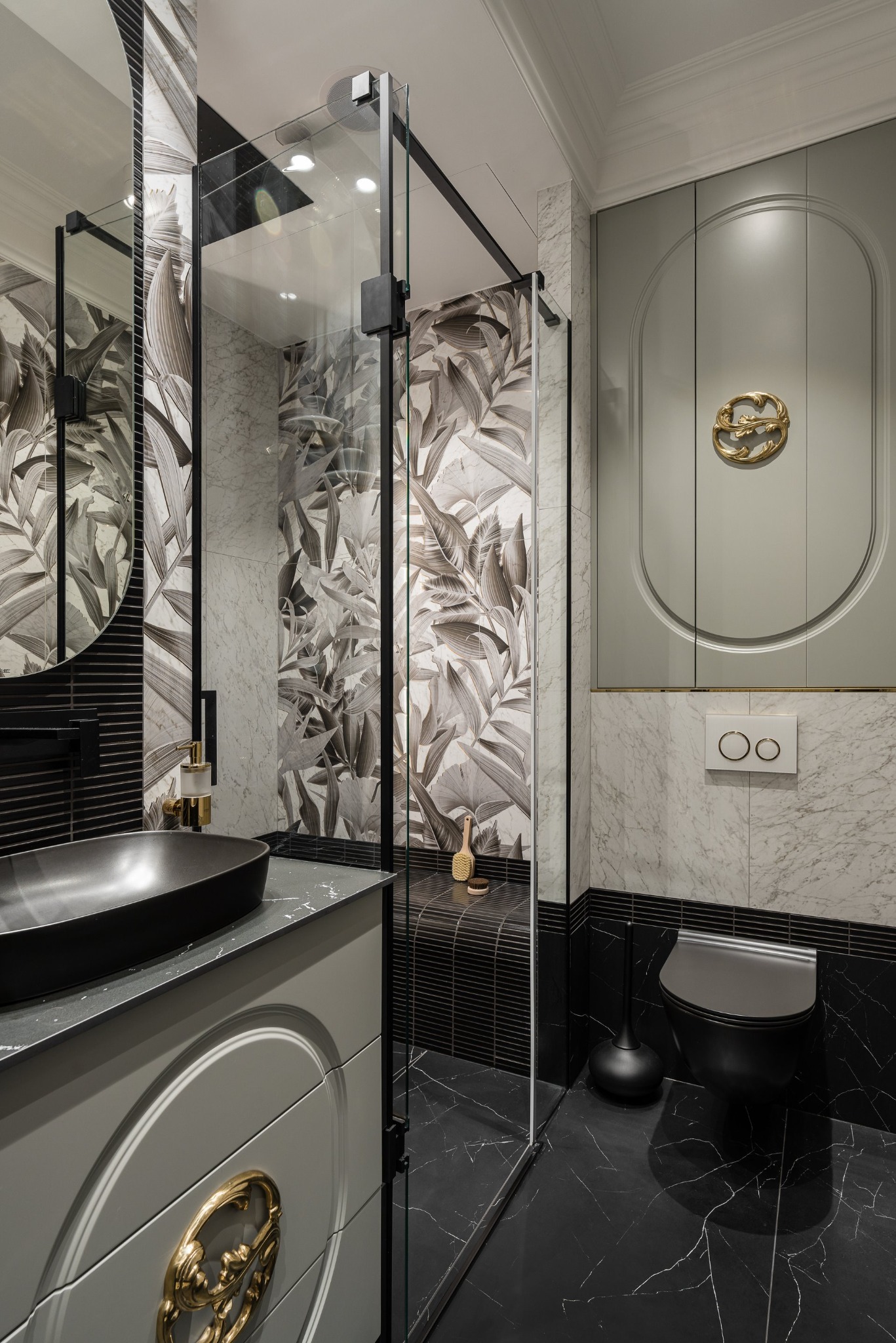 Elegancka łazienka z czarną umywalką na szafce z dekoracyjnym, złotym uchwytem, kabiną prysznicową i marmurowymi płytkami z motywem liści.