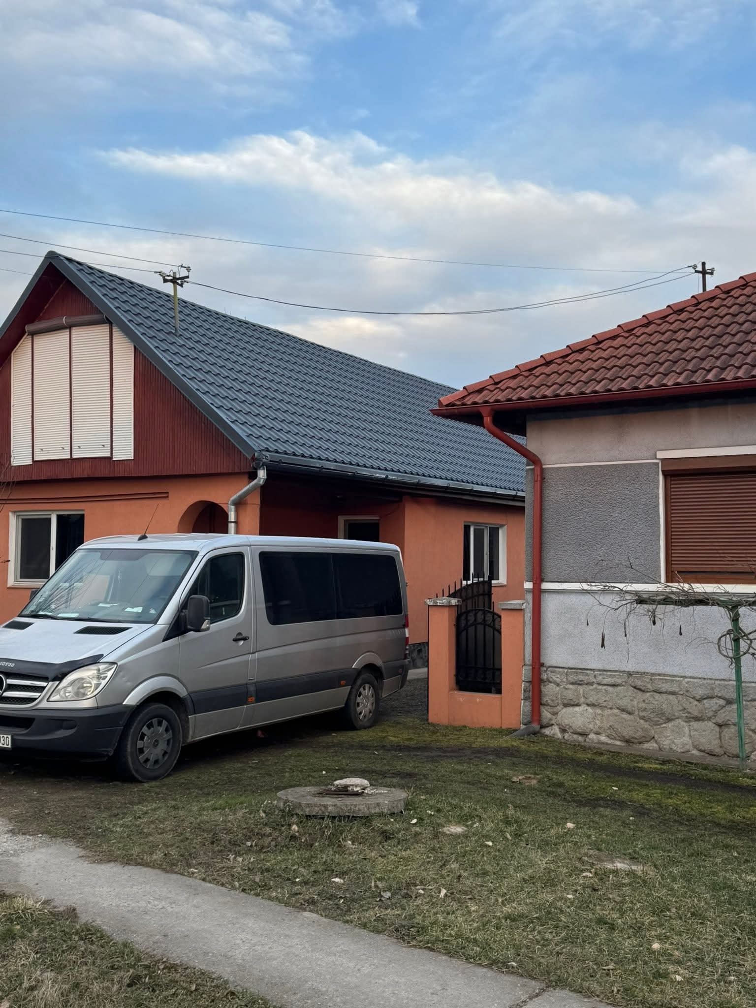 Dom z dwiema różnymi dachówkami i rynnami, obok zaparkowany srebrny bus. Widoczne elementy wykończenia dachu i orynnowania.