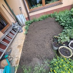 Piotr Ogrody - Przygotowane podłoże pod trawnik, z zachowanym pasem trawy na życzenie klienta. Widoczne narzędzia ogrodnicze i donice z roślinami. Ujęcie z góry.