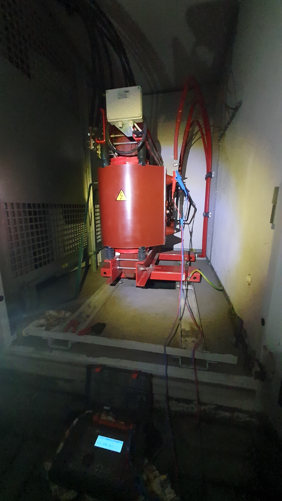 Transformator pomiarowy z podłączonym miernikiem w Sosnowcu. Czerwony cylinder z symbolem ostrzegawczym, kable i przewody. Pomiar elektryczny w pomieszczeniu.