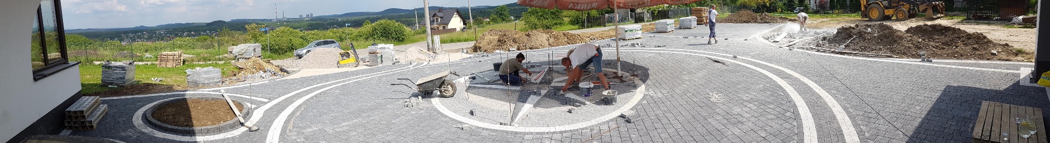 Trzebinia: Układanie kostki brukowej w okrągły wzór z białymi liniami. Widoczni pracownicy i materiały budowlane. Panorama z widokiem na okolicę.