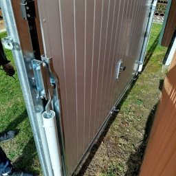 Henryk Rolka - Szczegółowe ujęcie mechanizmu prowadzącego przesuwnej bramy garażowej z widocznymi elementami montażowymi i fragmentem poszycia w kolorze jasnego beżu.