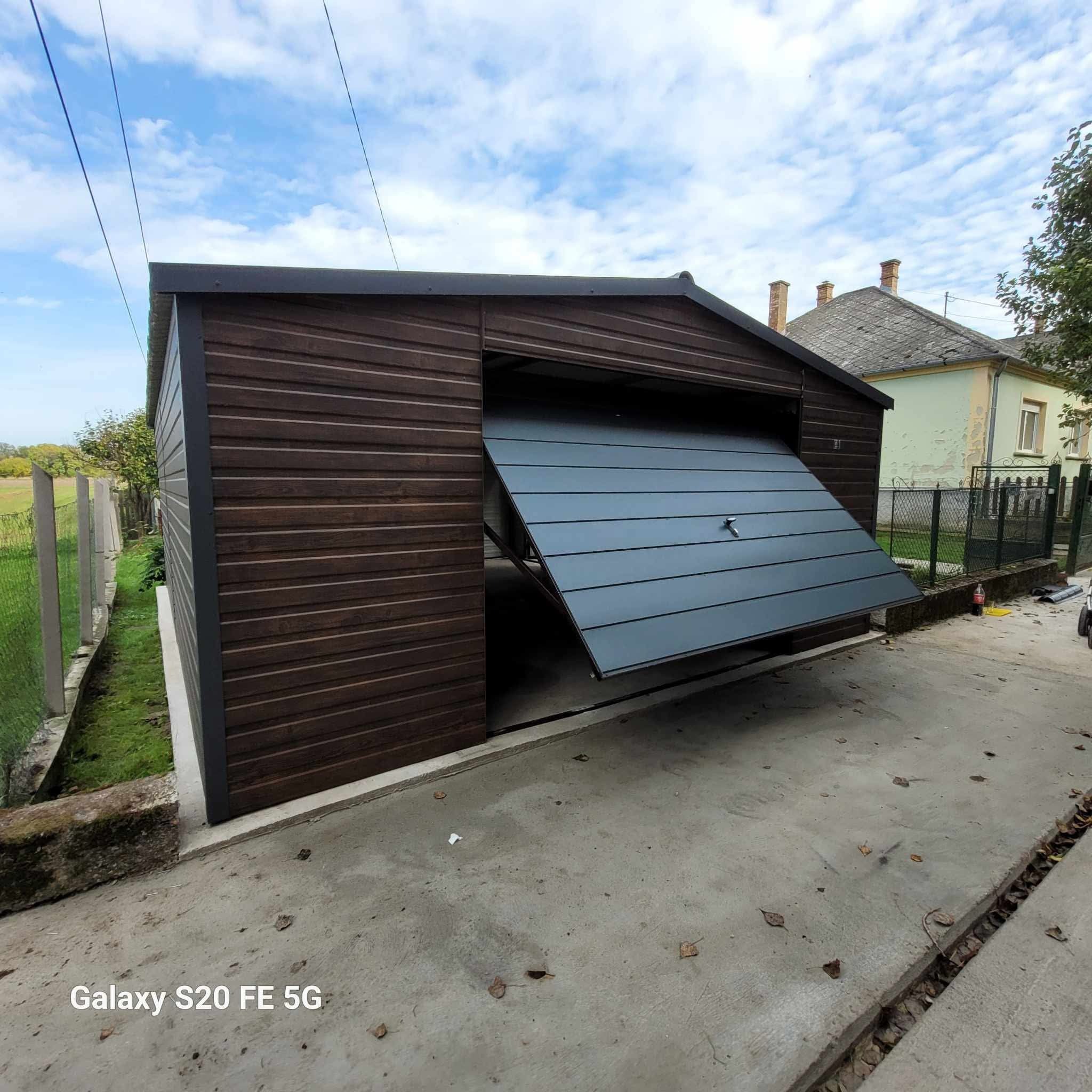 Drewniany garaż blaszany z uchyloną szarą bramą segmentową na betonowym podłożu. Widoczne detale konstrukcyjne i otoczenie posesji. Garaż z zewnątrz wykończony drewnem.