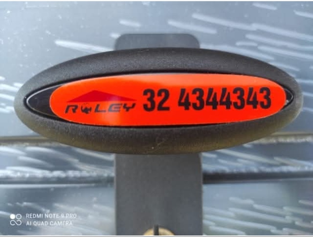 Detal bramy garażowej z numerem kontaktowym na pomarańczowej naklejce. Widoczny zamek i fragment konstrukcji bramy.