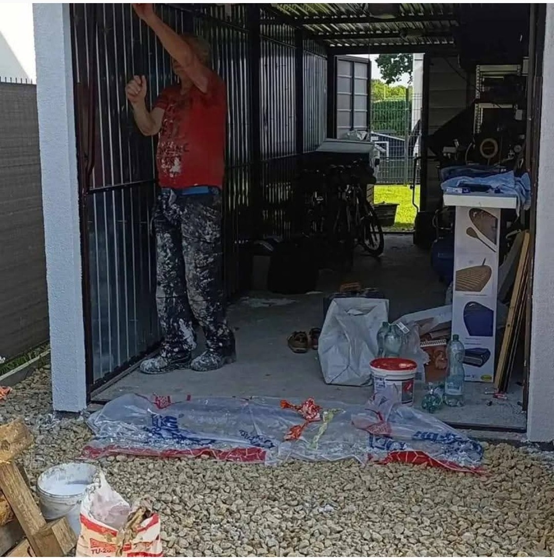 Malowanie bramy garażowej w Żorach. Mężczyzna w ubraniu roboczym maluje metalową konstrukcję na biało. Widoczne narzędzia i materiały malarskie.