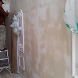 TYZON VICTOR TYSZLEWICZ - Prace malarskie w trakcie realizacji w Zabór Mały. Widoczna ściana z dekoracyjnymi elementami, malarz na drabinie i zabezpieczona podłoga.